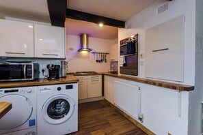 A compact kitchen with a washing machine, microwave, and oven. - Spacious 4-Bed House | Near Wigan & Warrington (Golborne)