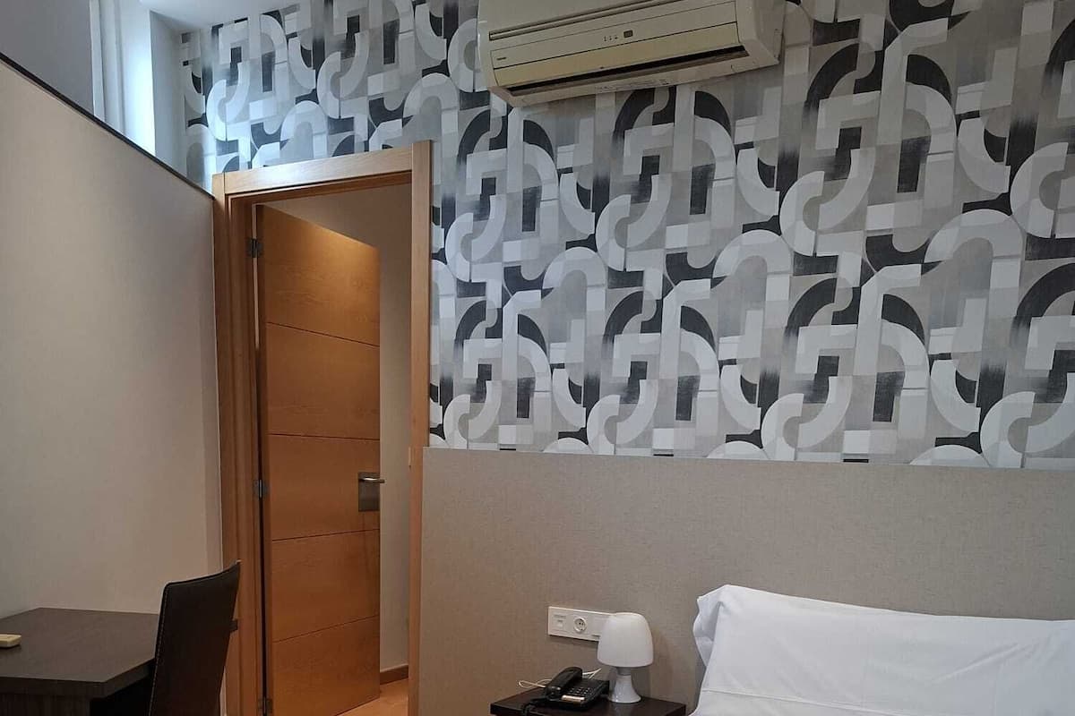 Une chambre d’hôtel comprenant un lit, un bureau, une chaise, une table de chevet avec une lampe et un appareil de climatisation.