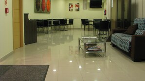 Un hall d’hôtel comprenant un comptoir d’accueil, un espace d’attente avec des chaises, un canapé, une table basse avec des magazines et un téléviseur fixé au mur.
