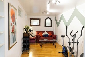 Ein Wohnzimmer mit einem roten Sofa, einem Glastisch, einem Heimtrainer und einem wandmontierten Spiegel.
