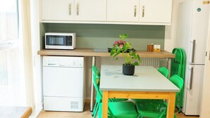 Cozinha compacta com armários brancos, micro-ondas, geladeira e uma mesa com cadeiras.