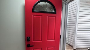 Una puerta roja con un picaporte negro y un panel de vidrio arriba.