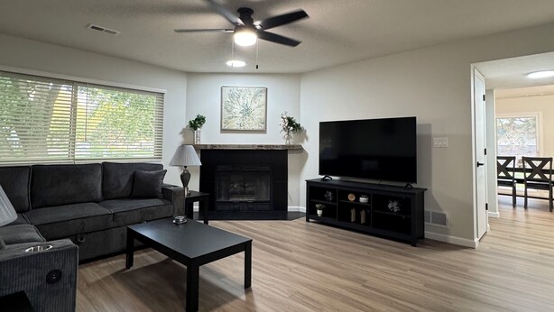 Una sala de estar con sofá, mesa de centro, televisor, chimenea y ventilador de techo.