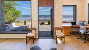 A room with a large window overlooking the beach, a desk with a laptop, and a seating area with a view. - Direct Beach Access!! - Casa On The Rocks Uruguay (Estación Las Flores)