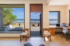 A room with a large window overlooking the beach, a desk with a laptop, and a seating area with a view. - Direct Beach Access!! - Casa On The Rocks Uruguay (Estación Las Flores)