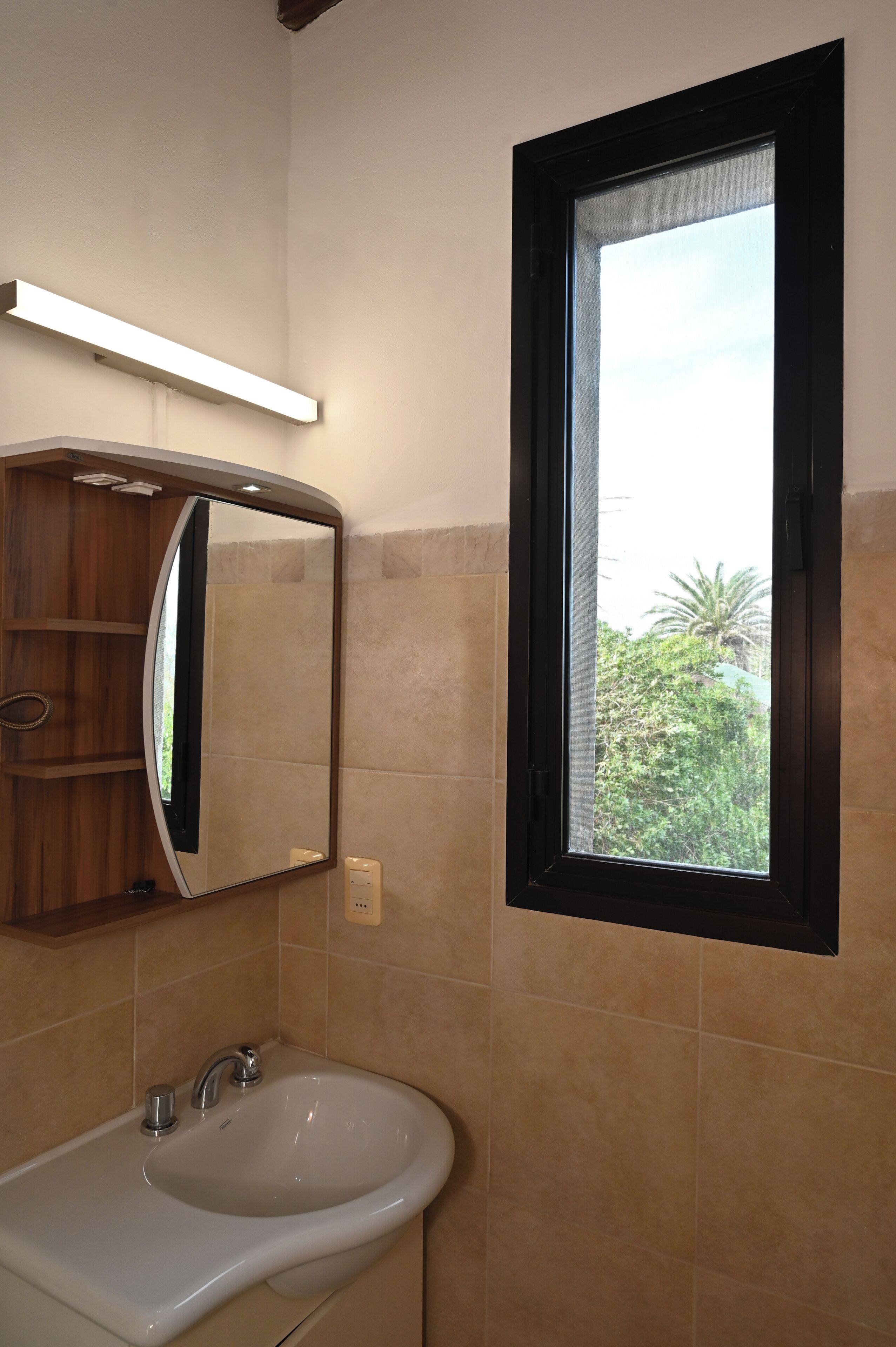 Une salle de bain avec un lavabo, un miroir et une fenêtre.