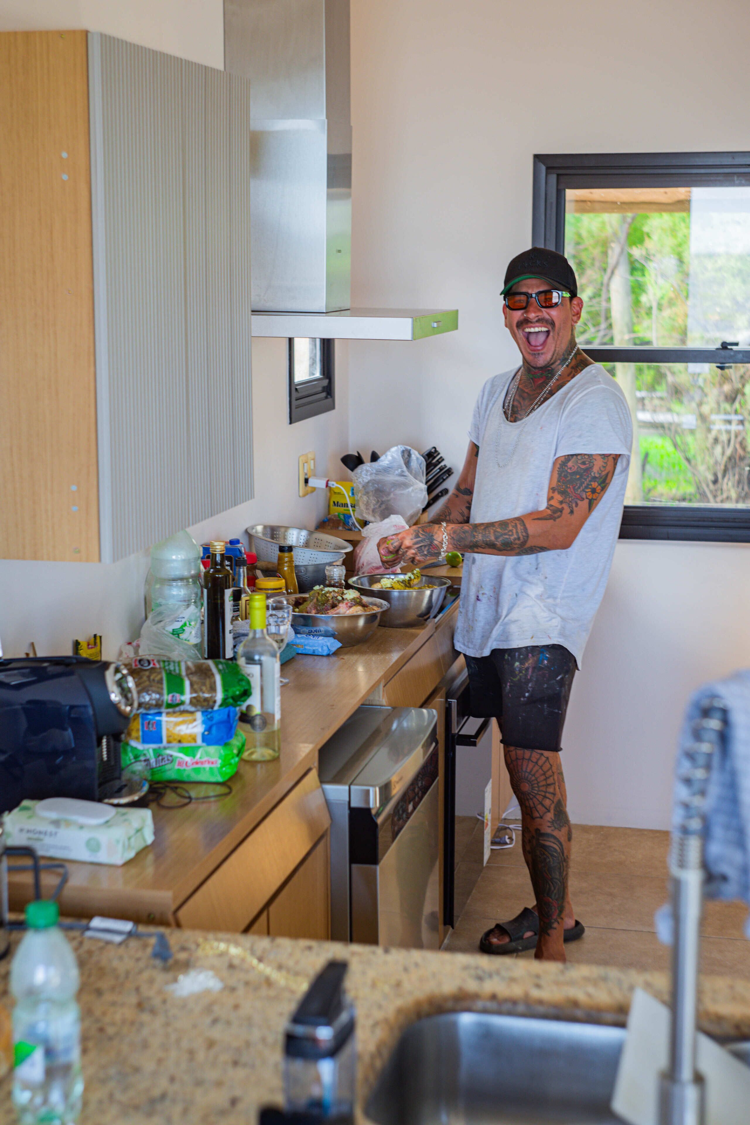 Eine Person bereitet Essen in einer Küche mit Fenster, Spüle und diversen Küchenutensilien auf der Arbeitsfläche zu.