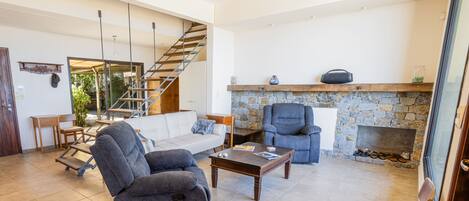 A spacious living area with a sofa, armchair, coffee table, fireplace, and a staircase.
