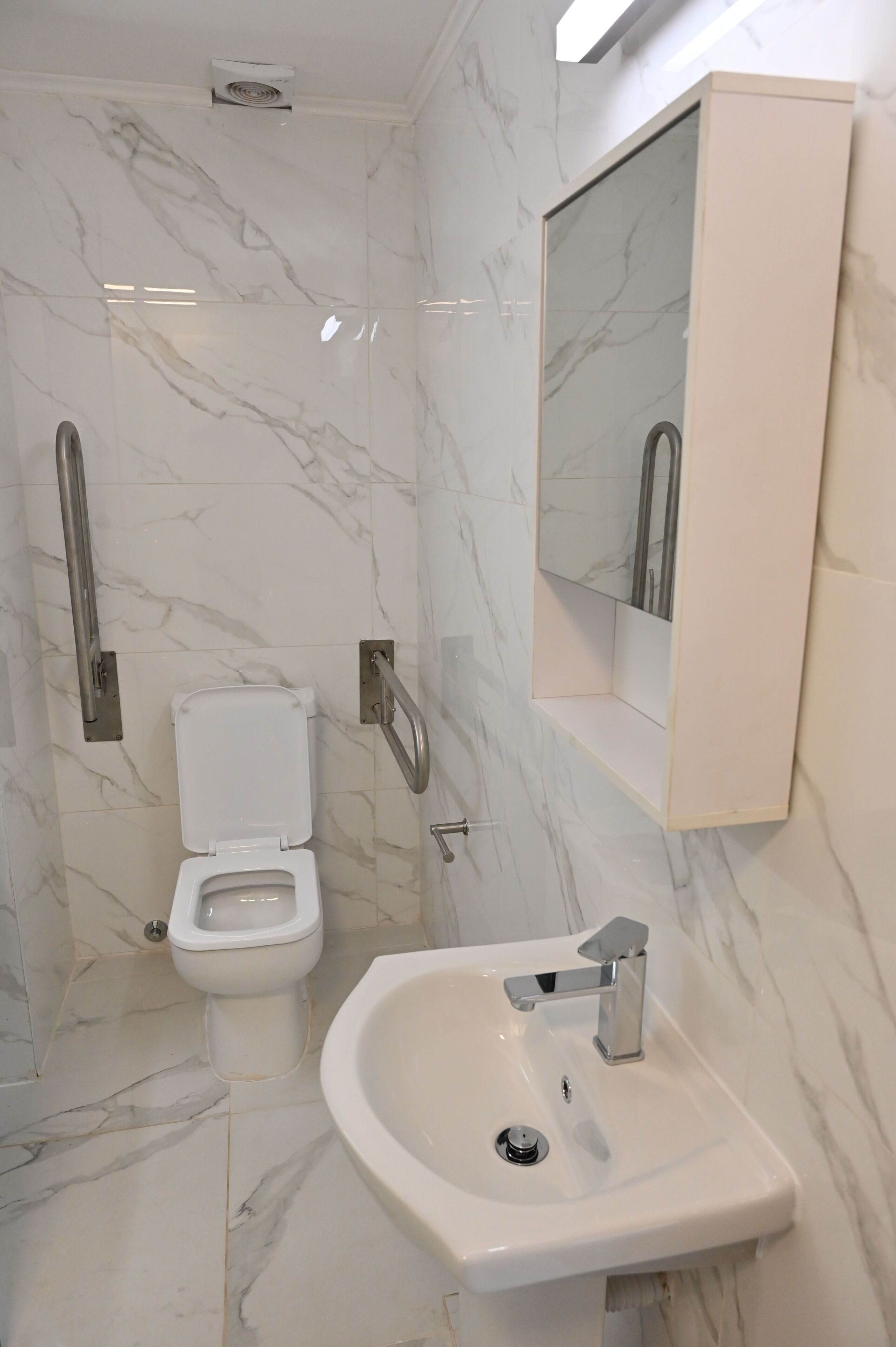 Un baño con inodoro, lavamanos, espejo y barandilla.