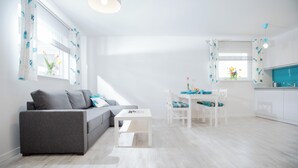 A modern living room with a grey sofa, a white coffee table, and a dining area with a white table and chairs. - Baltic Stone - Comfortable vacation homes in Rewal (Rewal)
