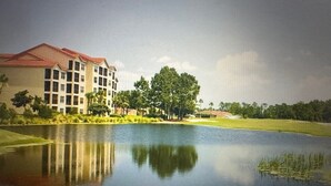Un resort con un edificio grande, una masa de agua y follaje circundante.