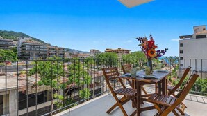 Ein Balkon mit Tisch und Stühlen, einem Blumenstrauß und Blick auf Gebäude und Grünflächen.