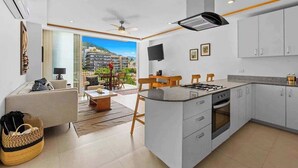 Eine moderne Küche mit Kochinsel, ein Essbereich mit Aussicht und ein Wohnbereich mit Sofa und Fernseher.
