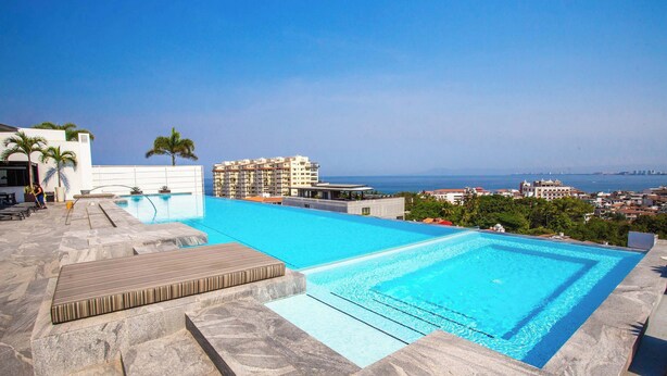 Ein Pool auf dem Dach mit klarem, blauem Wasser, einer Holzterrasse und Blick auf Stadt und Meer.