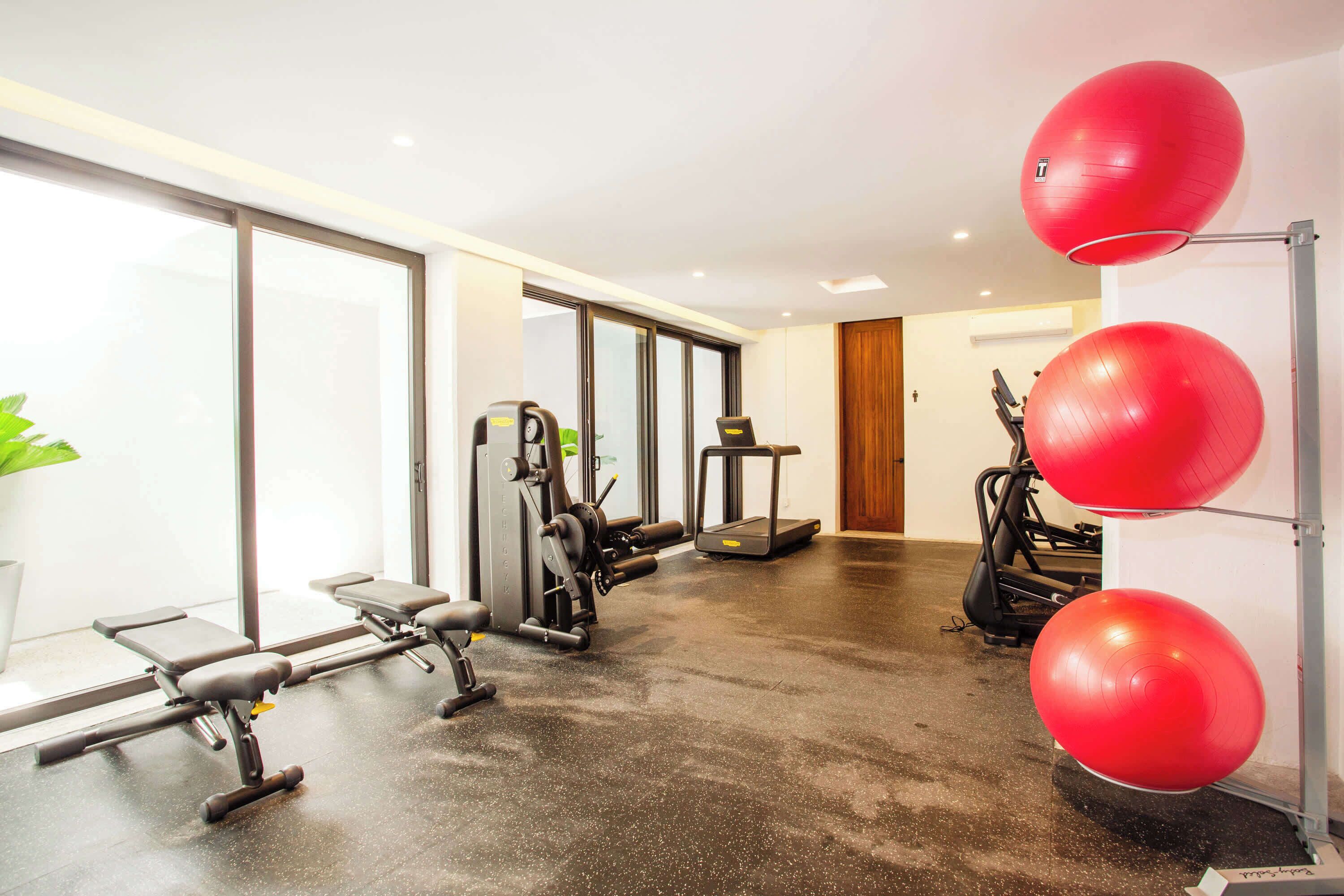 Un gimnasio con equipamiento de ejercicio, una cinta de correr y balones de ejercicio rojos.