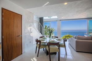 A modern dining area with a view of the ocean, a staircase, and a living room with a sofa. - Spectacular Casa de dos Davids (Puerto Vallarta)