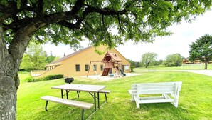 En plats för picknick med ett bord och en bänk, en träkonstruktion med en stege och en byggnad i bakgrunden.
