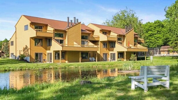 Ett hotell med flera våningar, ett platt tak, balkonger och en liten damm på förgrunden.