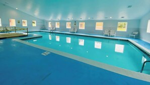 En inomhuspool med klart vatten, omgiven av vita stolar och fönster.