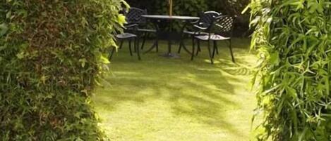 A garden with a table and chairs, surrounded by greenery.