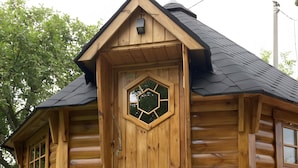 Une cabane en rondins de bois dotée d’une fenêtre hexagonale, d’une porte et d’un petit porche.
