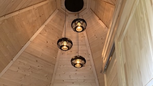 Un intérieur en bois avec un plafond en pente, trois luminaires suspendus, un lit avec un matelas blanc texturé et une petite table de chevet avec une lampe.