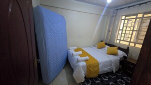 Een slaapkamer met een bed, een blauw matras, een raam met gordijnen en een kamerkleed met een patroon.