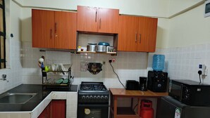 Een keuken met houten kastjes, een gasfornuis, een koffiezetapparaat, een waterdispenser en een koelkast.