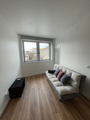 A room with a sofa, a window, and a black object on the floor. - Maria do Carmo – Casa das Gatas (Pombal)
