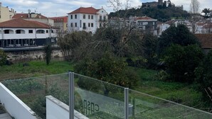 Balcón con barandilla de vidrio que da a una zona residencial, un campo cubierto de hierba y una estructura distante con aspecto de castillo.