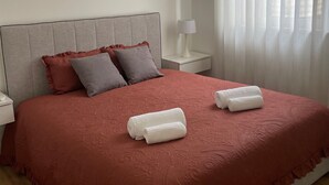 Una cama bien hecha con una colcha roja, dos almohadas y dos toallas enrolladas.