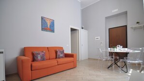 A living room with a sofa, a dining table with chairs, a door, and a wall-mounted painting. - Abbi's House - Apartment in the Historic Center of Naples (Napoli)