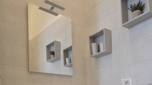 A modern bathroom with a built-in sink, a mirror, and a small shelf with toiletries. - Abbi's House - Apartment in the Historic Center of Naples (Napoli)