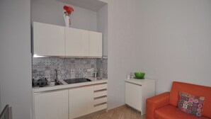 A compact kitchen with white cabinets, a patterned backsplash, a small countertop, and a green bowl on a white cabinet. - Abbi's House - Apartment in the Historic Center of Naples (Napoli)