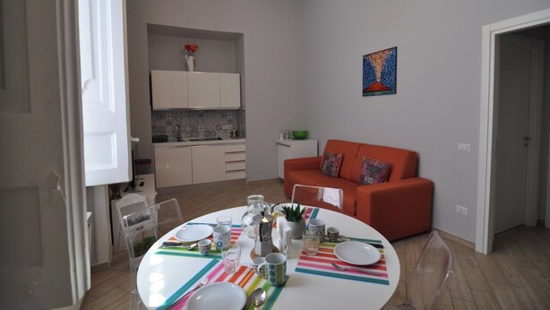 A modern living room with a dining table set for four, a kitchen with white cabinets, and a red sofa. - Abbi's House - Apartment in the Historic Center of Naples (Napoli)