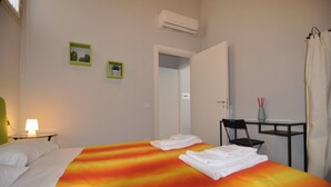A hotel room with a bed, a desk, a chair, a lamp, and two framed pictures on the wall. - Abbi's House - Apartment in the Historic Center of Naples (Napoli)