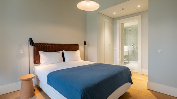 A modern bedroom with a large bed, a bedside table, a hanging light fixture, and a door leading to a bathroom. - FLH Heart of Rossio Apartment X (Lisboa ciudad)