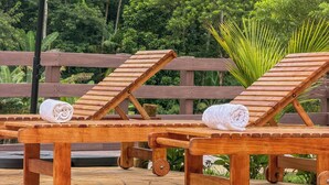 A wooden deck with two lounge chairs, each with a towel, under a red umbrella. - Villa Mantiqueira SFX - Suítes (São José dos Campos)