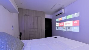 Une chambre à coucher comprenant un lit, une armoire et un projecteur fixé au mur, qui diffuse des services de diffusion en continu.