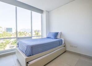 Ein modernes Schlafzimmer mit großem Fenster, einem Bett mit blauer Bettdecke und einer weißen Wand.