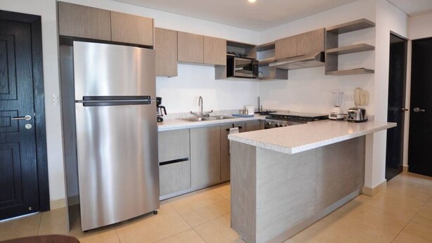 Une cuisine moderne dotée d’un réfrigérateur en acier inoxydable, de meubles en bois, d’un îlot central et d’un four à micro-ondes placé au-dessus de la cuisinière.