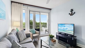 En moderne stue med sofa, sofabord i glas, fjernsyn og en balkon med udsigt.