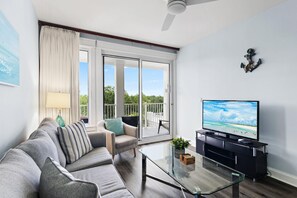 Ein modernes Wohnzimmer mit einer Couch, einem Glastisch, einem Fernseher und einem Balkon mit Blick.
