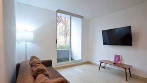 A modern living room with a sofa, a flat-screen TV, a small table, and a large window. - Zona Médica - Christus Muguerza - 2 Rec / 2 baños (Monterrey)