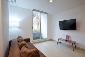 Un salon moderne avec un canapé, un téléviseur à écran plat, une petite table et une grande fenêtre.