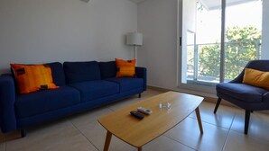Uma sala de estar com um sofá azul, uma mesa de centro de madeira, um abajur e uma cadeira.