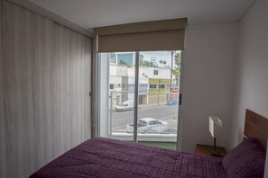 Une chambre d’hôtel avec un lit, une table de chevet, une lampe et une fenêtre donnant sur les bâtiments et les voitures à l’extérieur.