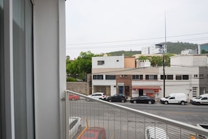 Une vue depuis un balcon donnant sur une rue bordée d’immeubles, avec des voitures et une colline en arrière-plan.