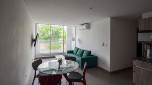 Un salon moderne avec une table à manger en verre, un canapé de couleur turquoise et une grande fenêtre donnant sur un paysage verdoyant.