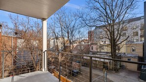 A balcony with a metal railing overlooking a cityscape with buildings and bare trees.